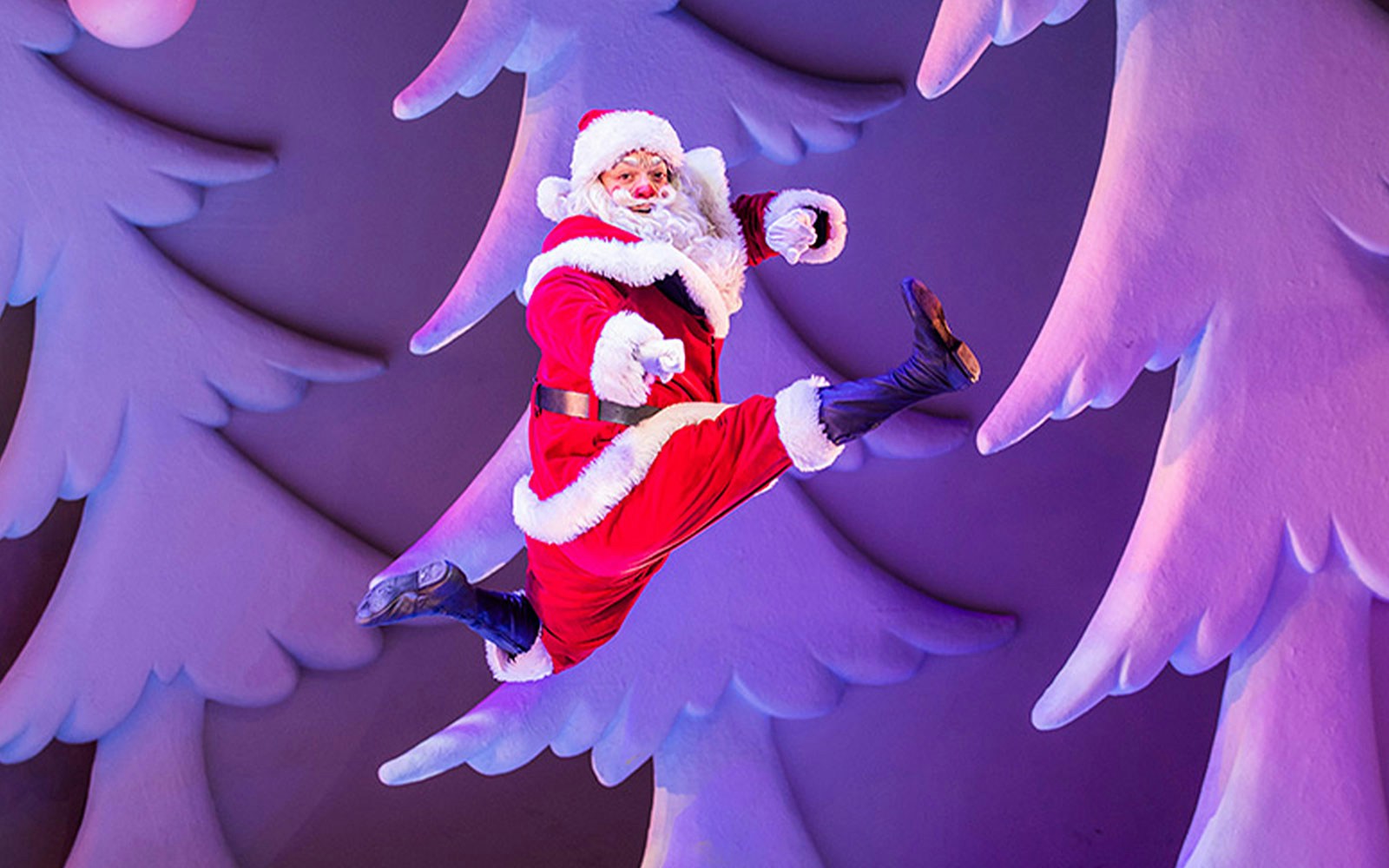 Santa Claus leaping in front of snowy trees during The Snowman show.