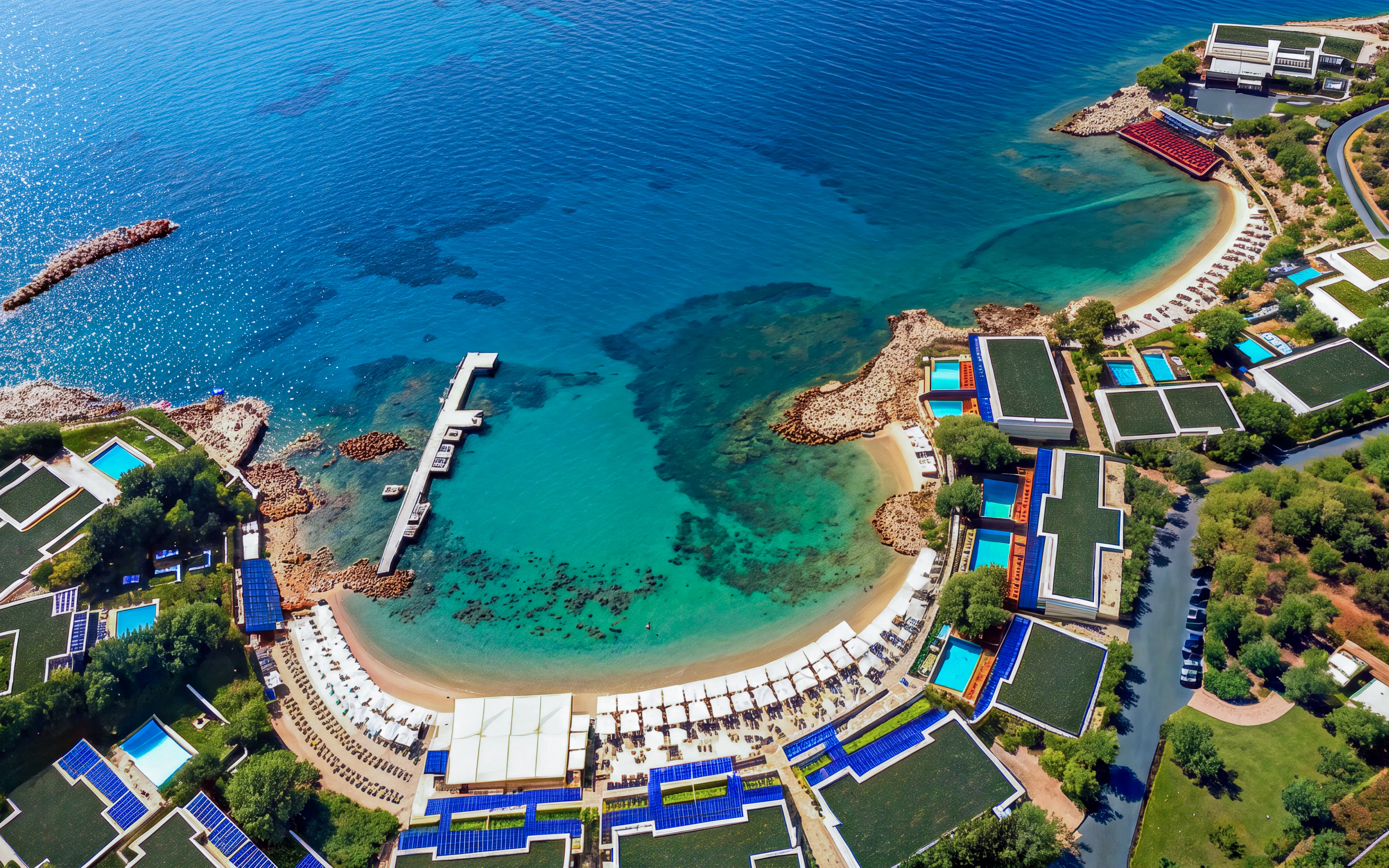 Aerial view of a coastal resort with a pier and clear blue waters in Sounion, Greece.