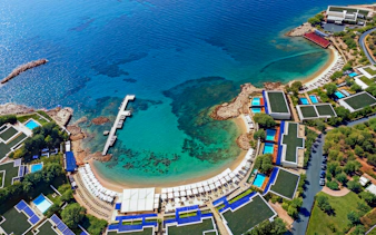 Aerial view of a coastal resort with a pier and clear blue waters in Sounion, Greece.