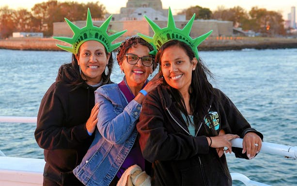 Family wearing Statue of Liberty crowns on a boat with Liberty Island in the background.