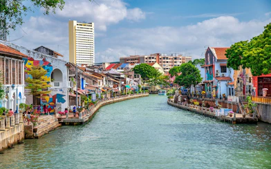 Melaka River with colorful buildings and murals on a sunny day.