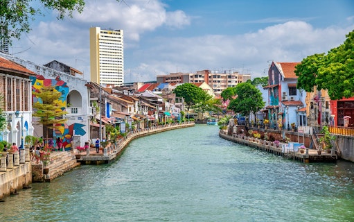 Melaka River with colorful buildings and murals on a sunny day.