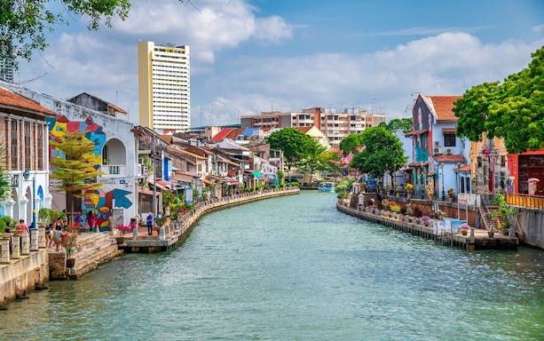 Melaka River with colorful buildings and murals on a sunny day.