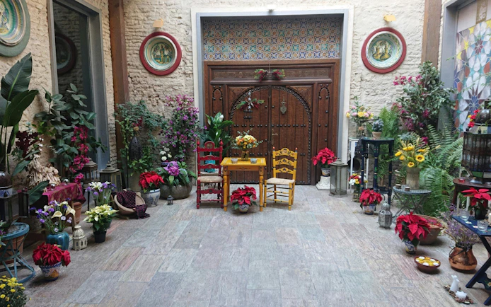 Tablao Casa de la Memoria courtyard with colorful chairs, flowers, and ornate wooden door.