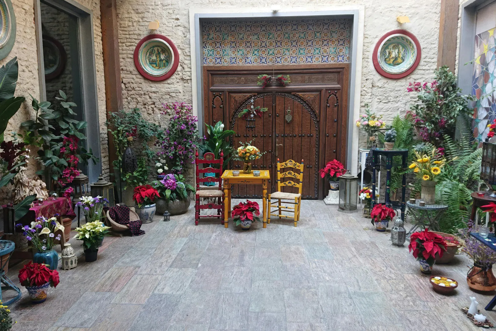Tablao Casa de la Memoria courtyard with colorful chairs, flowers, and ornate wooden door.