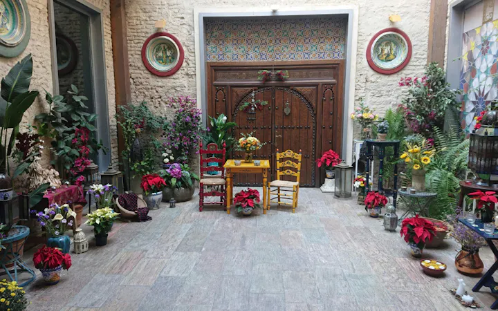 Tablao Casa de la Memoria courtyard with colorful chairs, flowers, and ornate wooden door.