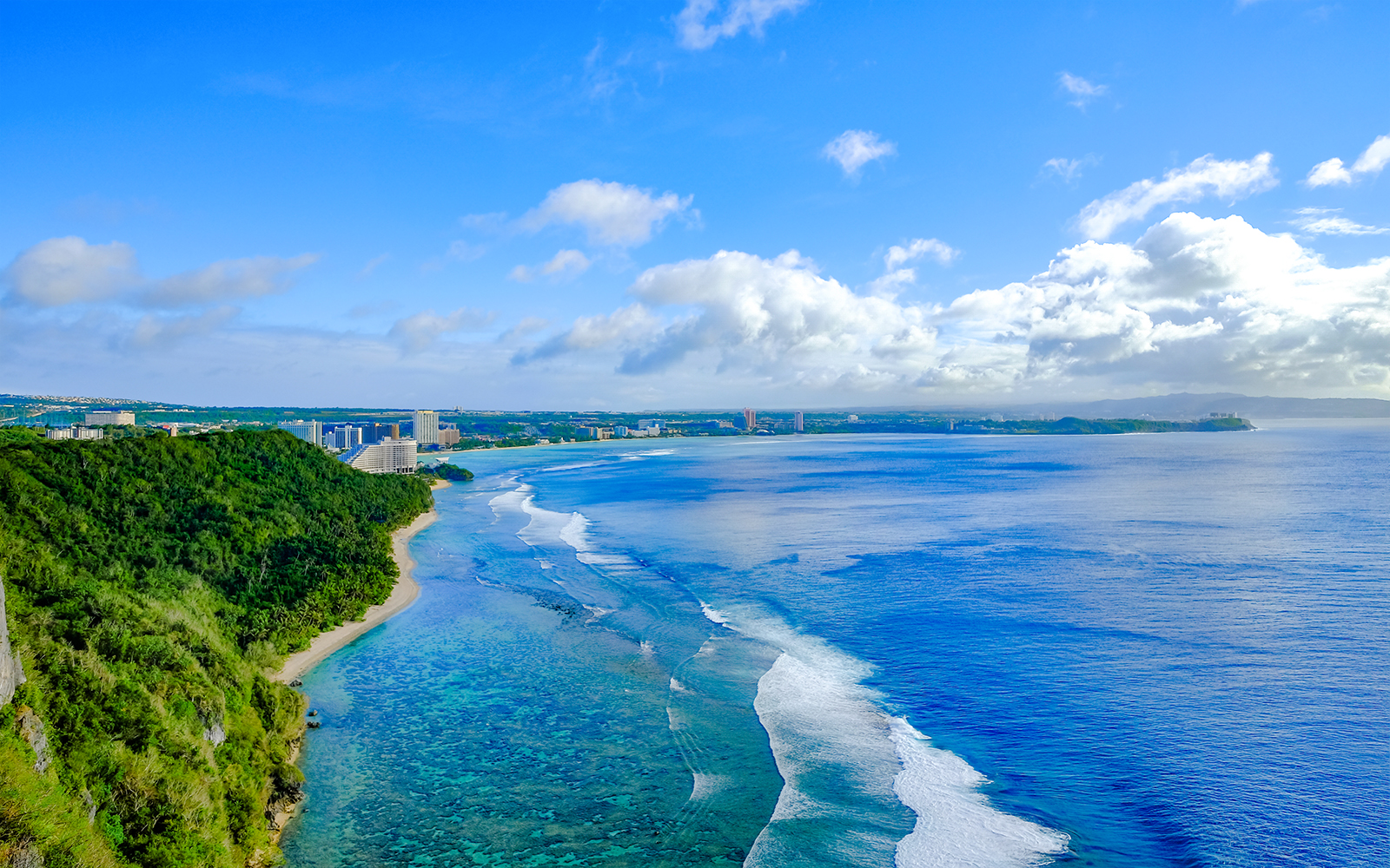 Tumon Bay Beach, Guam with tourists enjoying the clear blue water and sandy shoreline.