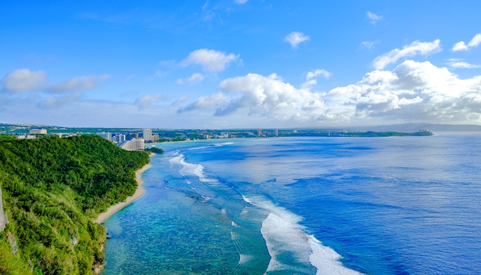 Tumon Bay Beach, Guam with tourists enjoying the clear blue water and sandy shoreline.
