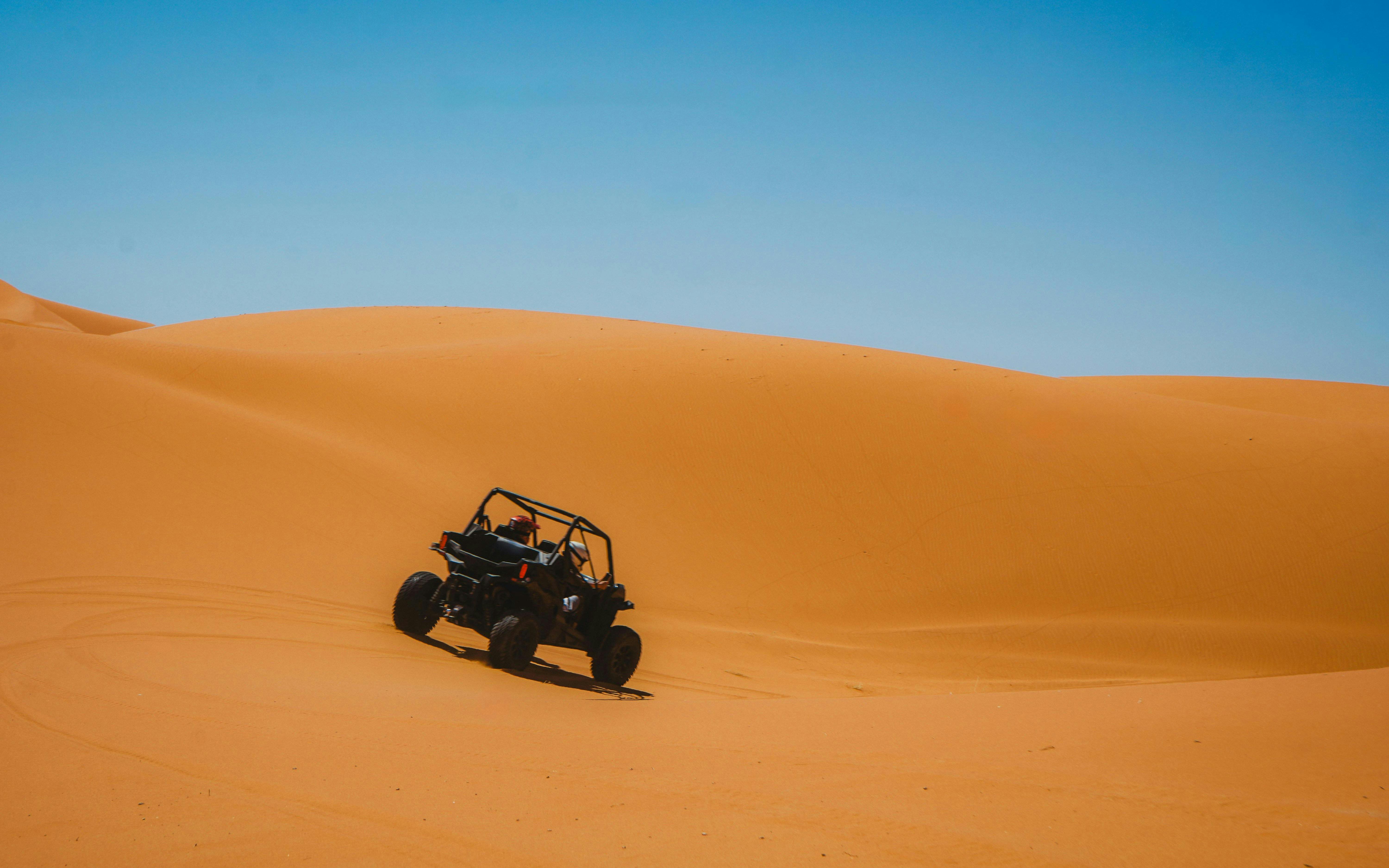 Buggy driving through golden desert dunes under clear blue sky.