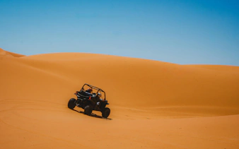 Buggy driving through golden desert dunes under clear blue sky.