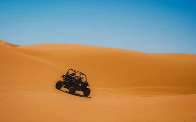 Buggy driving through golden desert dunes under clear blue sky.