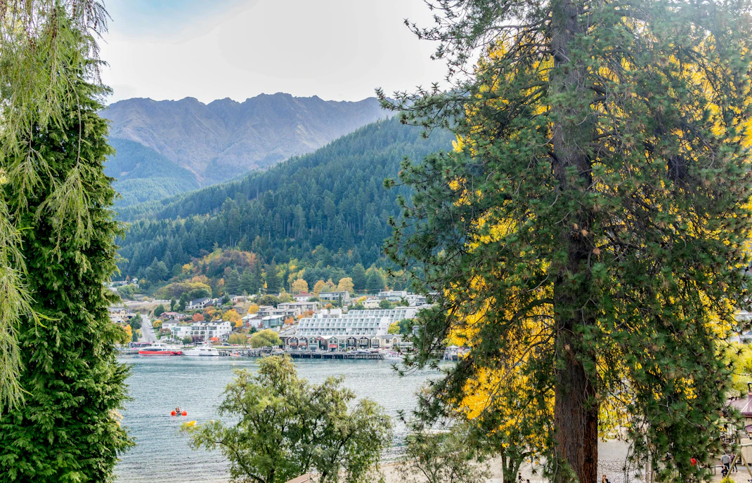 View of Steamer Wharf across Lake Wakatipu framed by trees in Queenstown Gardens.