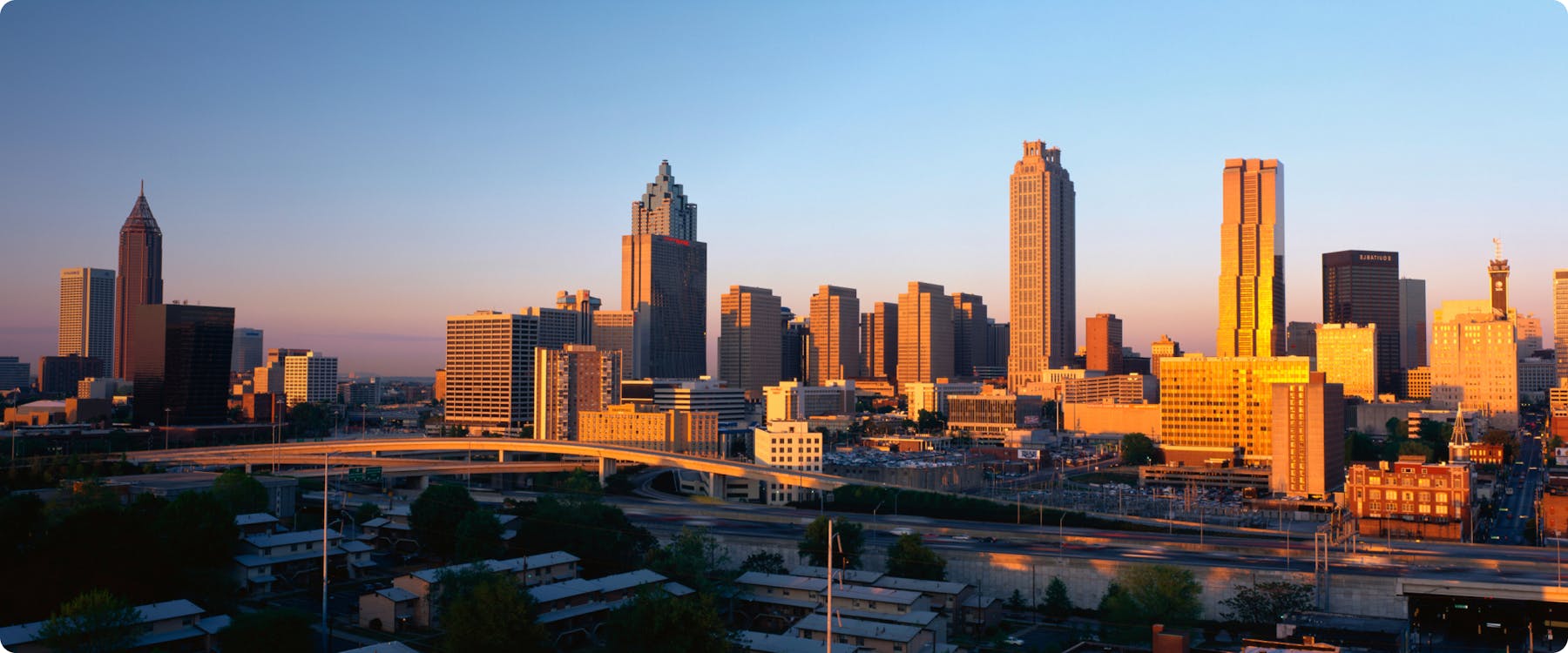 Atlanta skyline at sunset with prominent skyscrapers and highway in foreground.