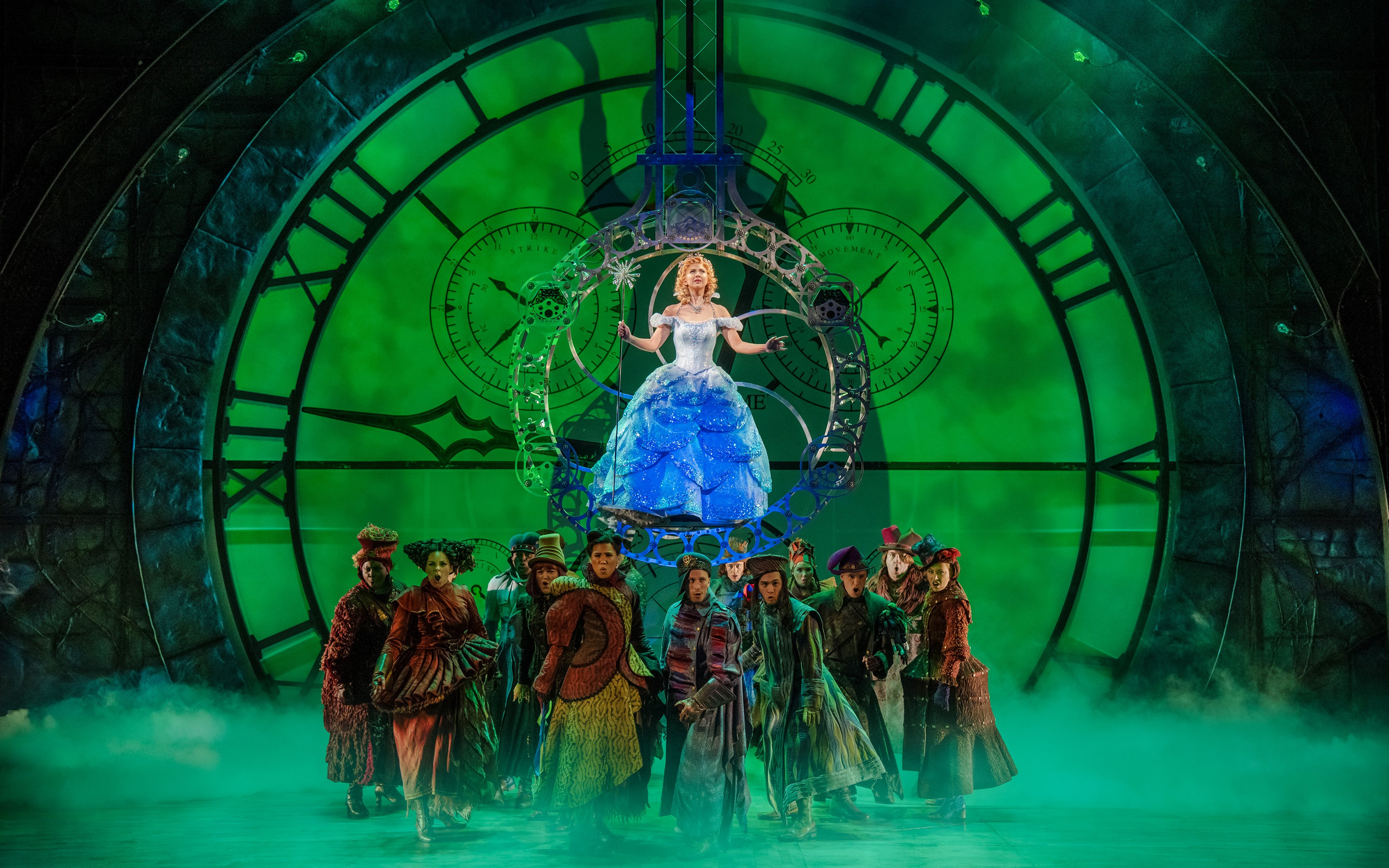 Stage scene from the musical Wicked with performers in front of a large clock.