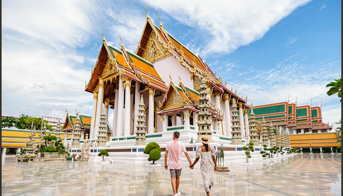 Couple walking towards Wat Suthat Thepwararam temple in Bangkok, Thailand.