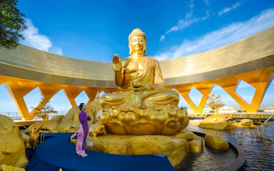 Golden Buddha statue at Cao Dai Holy See, Tay Ninh, with visitor in traditional attire.