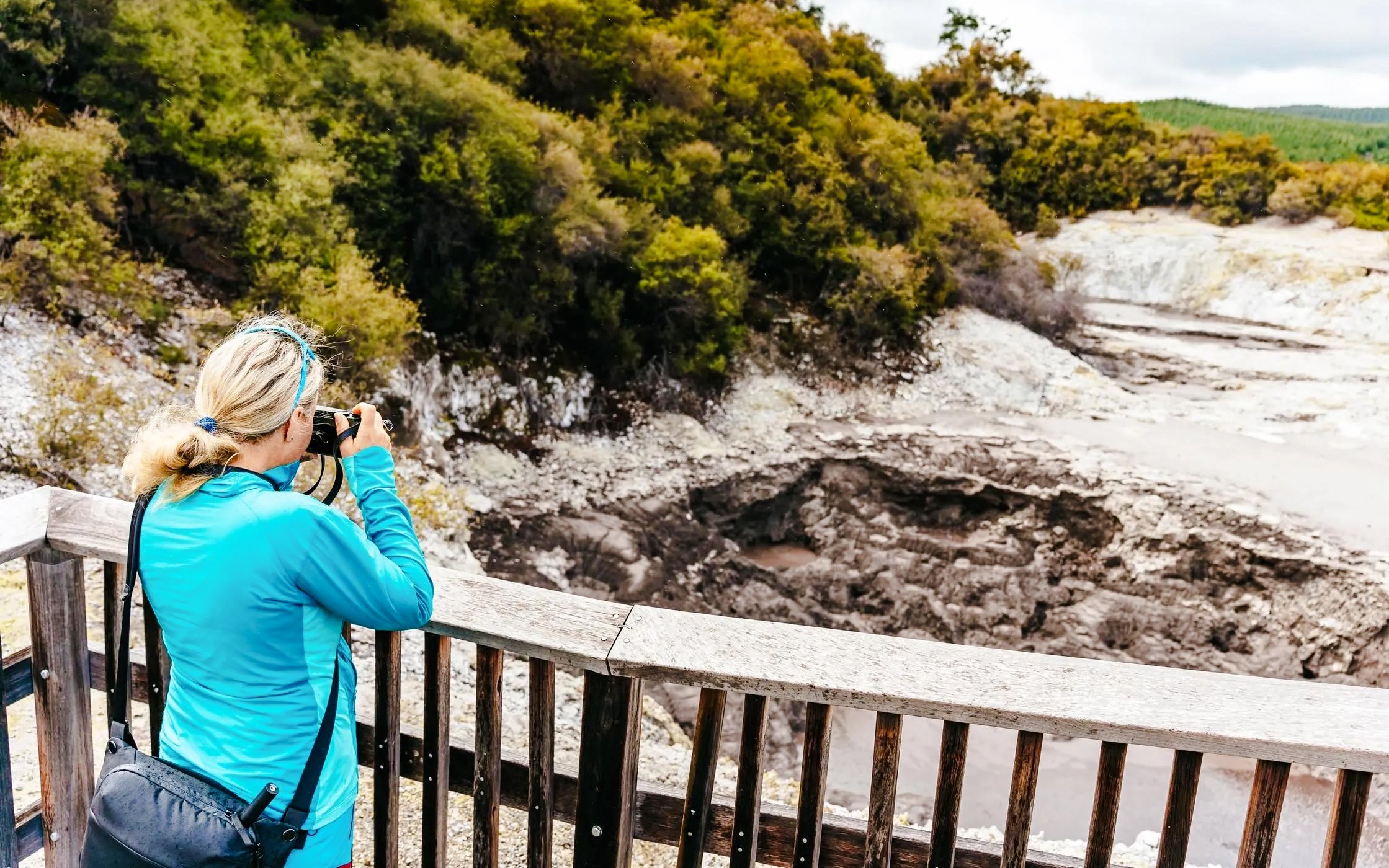 Visitor photographing geothermal landscape at Wai-O-Tapu Thermal Wonderland, New Zealand.