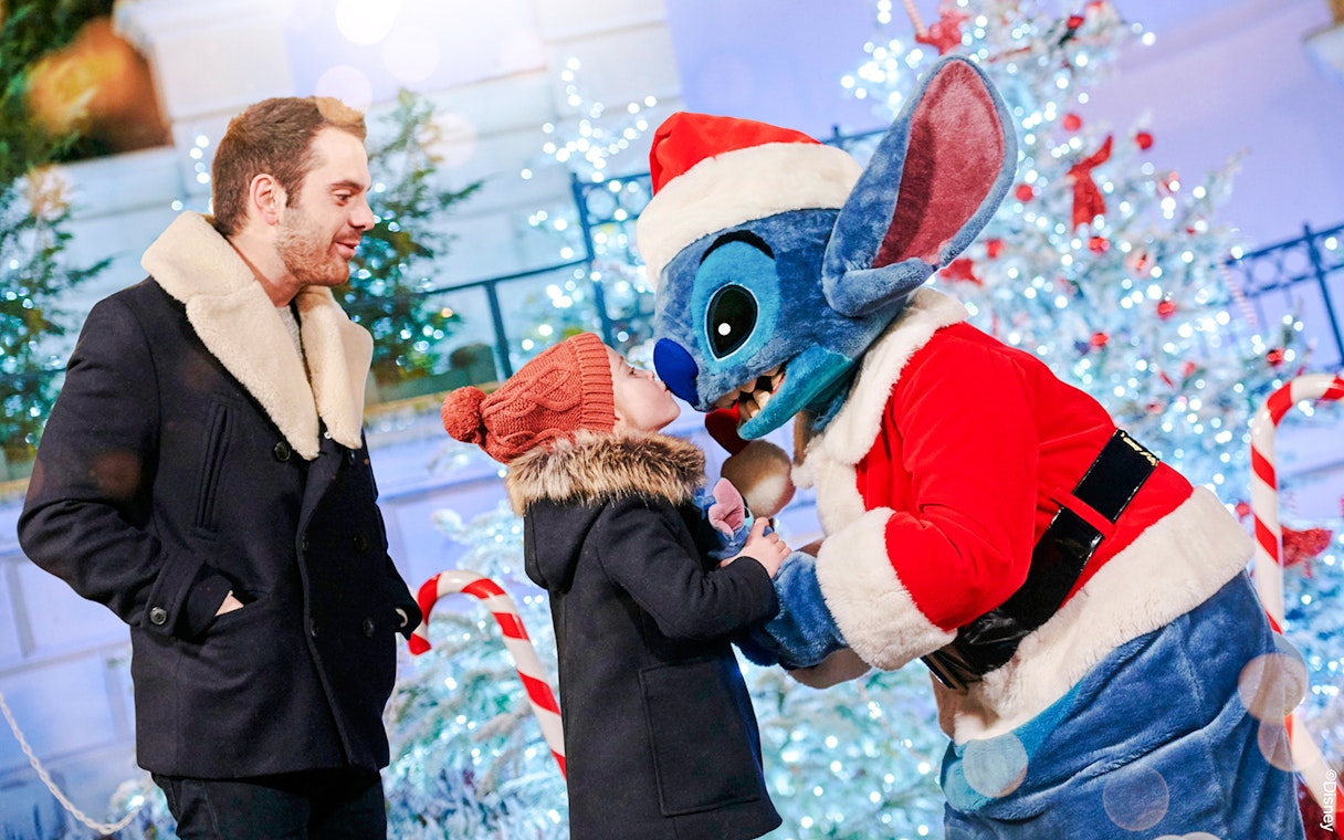Stitch in Santa outfit greeting child at Disneyland Christmas 2025 celebration.