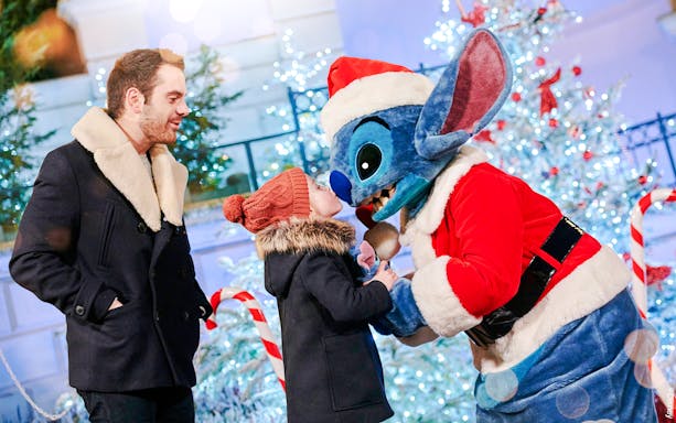 Stitch in Santa outfit greeting child at Disneyland Christmas 2025 celebration.