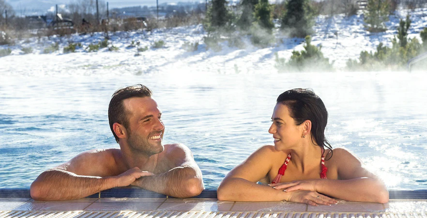 Tourists relaxing in a thermal spa with snowy Zakopane mountains in the background.