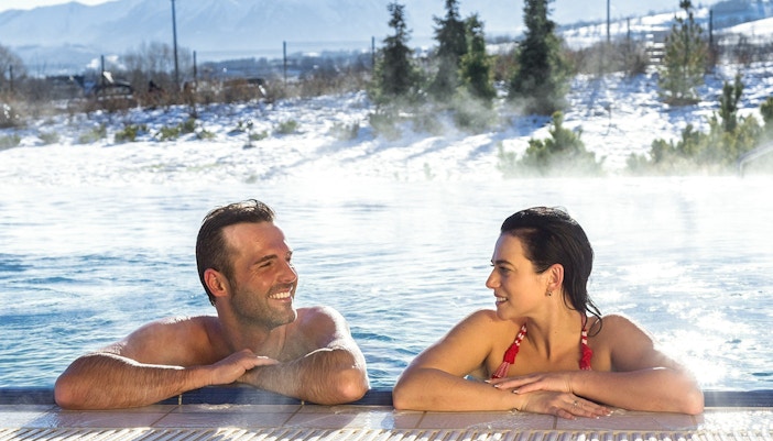 Tourists relaxing in a thermal spa with snowy Zakopane mountains in the background.