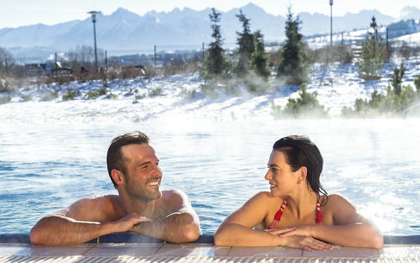 Tourists relaxing in a thermal spa with snowy Zakopane mountains in the background.