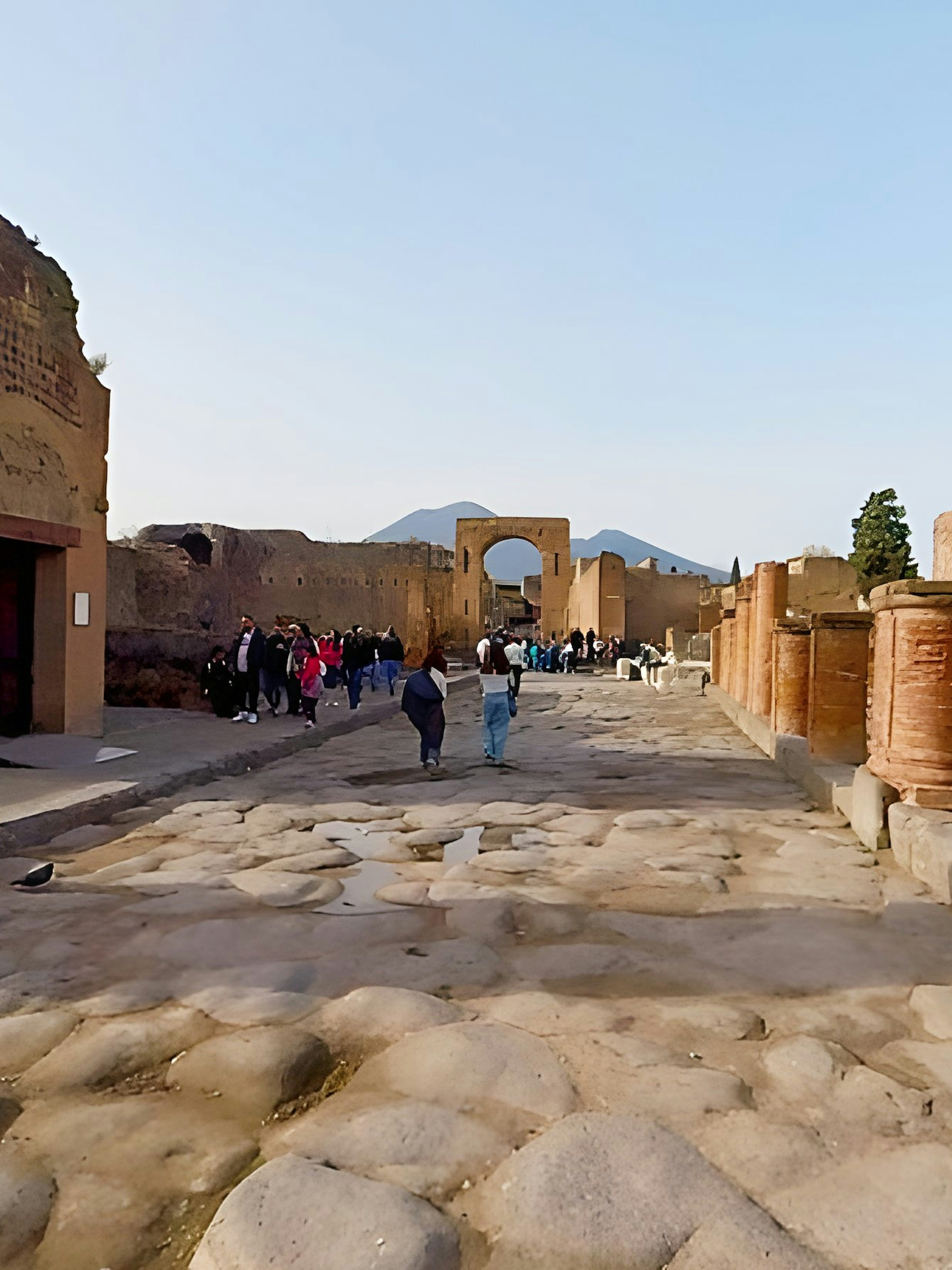 Tourists exploring the ancient streets of Pompeii, Italy, with Mount Vesuvius in the background.