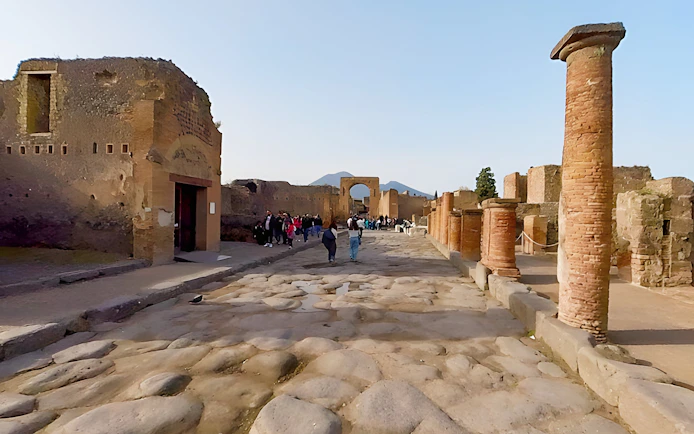 Tourists exploring the ancient streets of Pompeii, Italy, with Mount Vesuvius in the background.