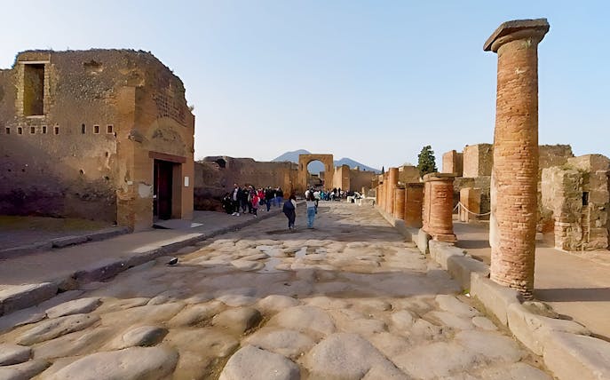 Tourists exploring the ancient streets of Pompeii, Italy, with Mount Vesuvius in the background.