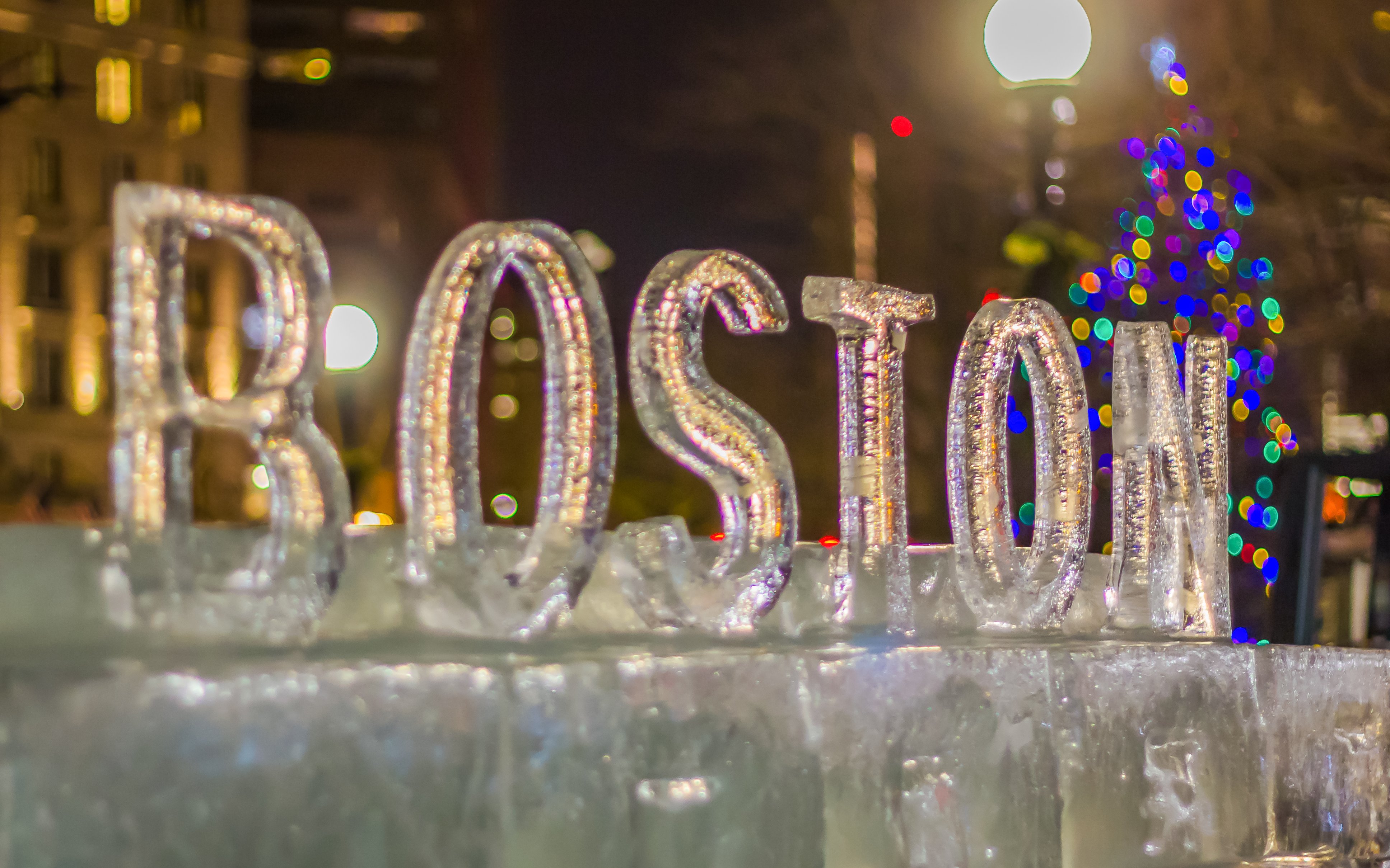 Boston ice sculpture with colorful lights in the background during New Year celebrations.