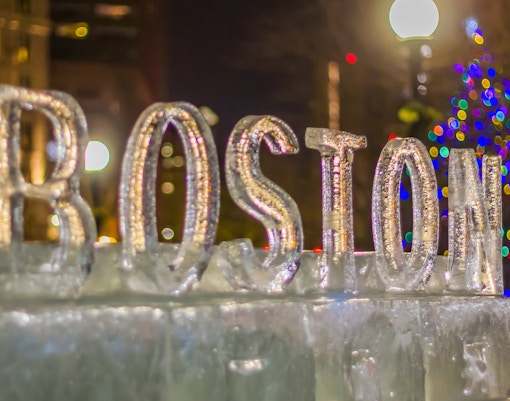 Boston ice sculpture with colorful lights in the background during New Year celebrations.