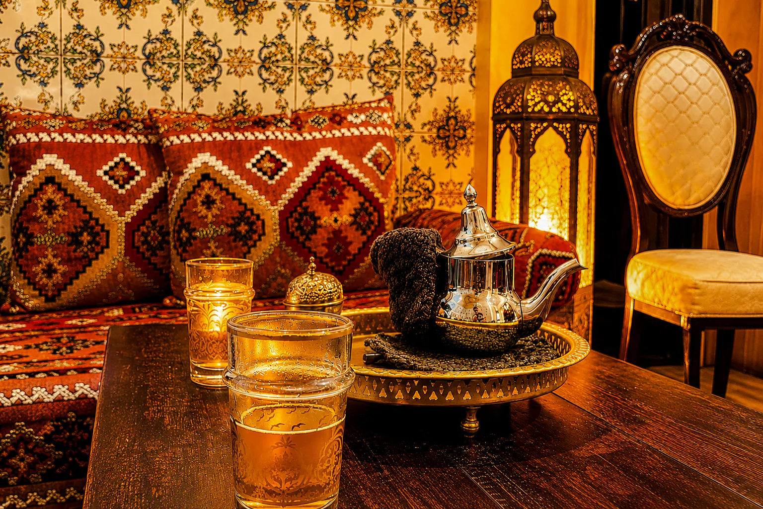 Moroccan tea set on a table with ornate cushions and lantern in Marrakesh hammam.