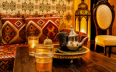 Moroccan tea set on a table with ornate cushions and lantern in Marrakesh hammam.