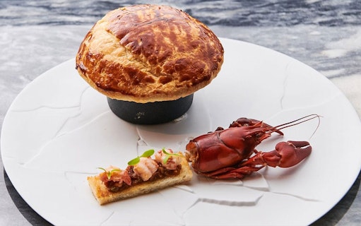 Wagyu beef pie with lobster and toast on a white plate.