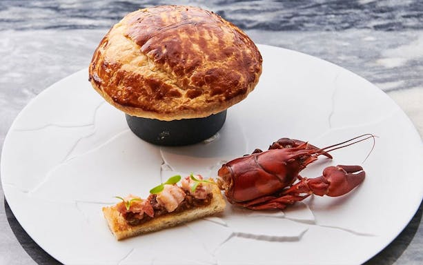 Wagyu beef pie with lobster and toast on a white plate.