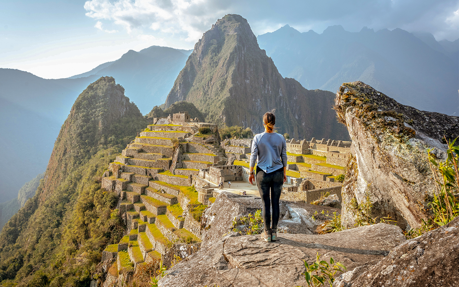 Person overlooking Machu Picchu ruins in Peru with Huayna Picchu mountain in the background.