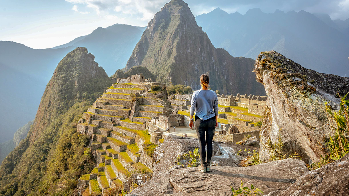 Person overlooking Machu Picchu ruins in Peru with Huayna Picchu mountain in the background.