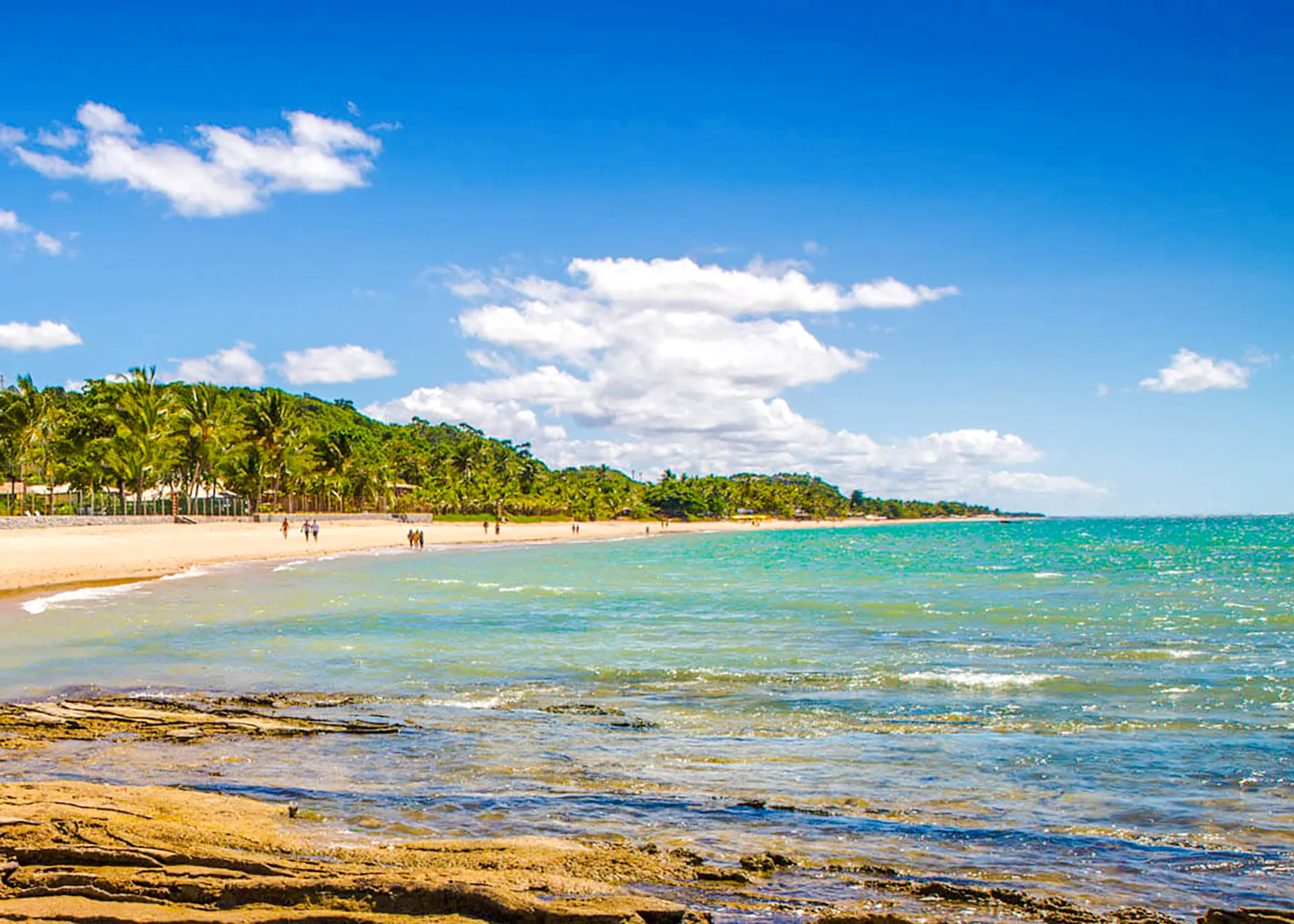 Beach view at Arraial d'Ajuda, Porto Seguro, with palm trees and clear blue water.