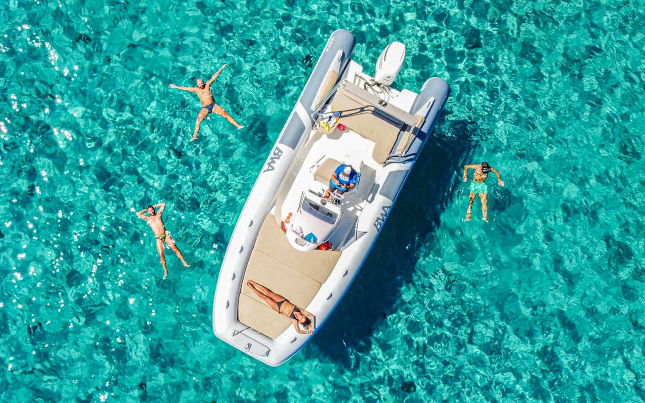 Boat with people swimming in clear blue waters during a Gulf of Cagliari tour.