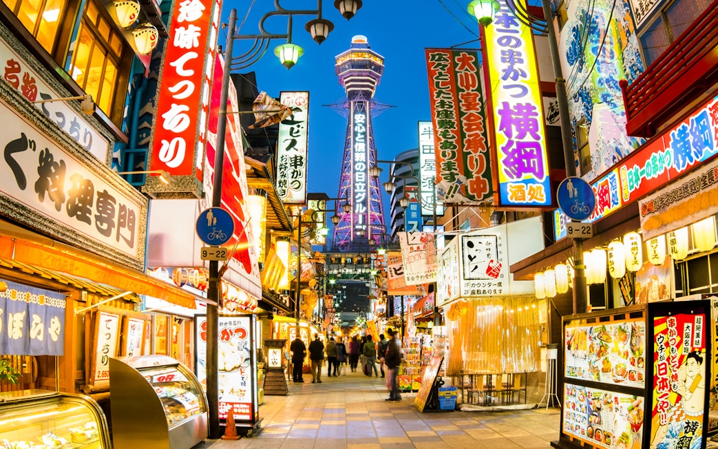 Bustling street in Osaka with Tsutenkaku Tower in the background.