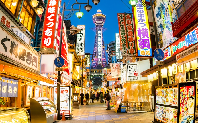 Bustling street in Osaka with Tsutenkaku Tower in the background.