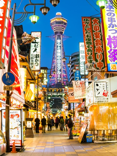 Bustling street in Osaka with Tsutenkaku Tower in the background.