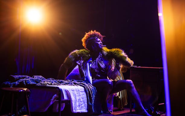 Performer on stage under spotlight, wearing a fur-trimmed coat, related to Lempicka.