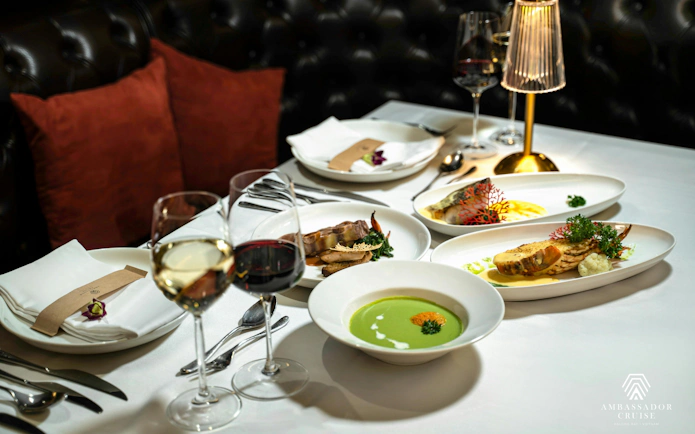 Fine dining setup on Ha Long Bay 5-Star Ambassador Cruise with gourmet dishes and wine glasses.