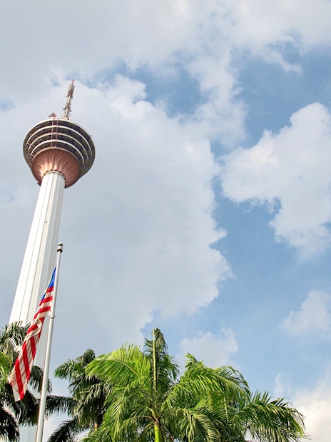 KL Tower in Kuala Lumpur with palm trees and Malaysian flag in foreground.