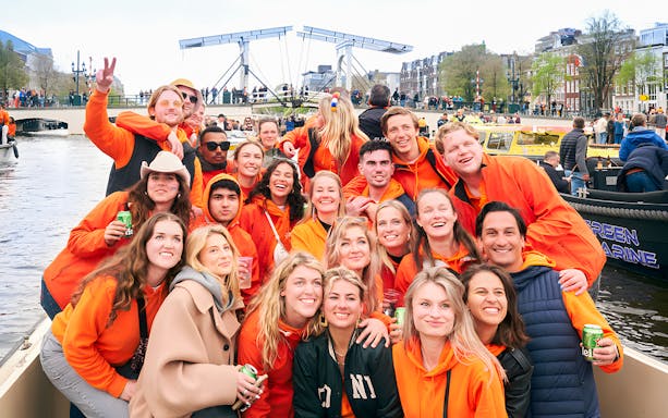 Group celebrating on a boat during Amsterdam King's Day cruise with open bar and music.