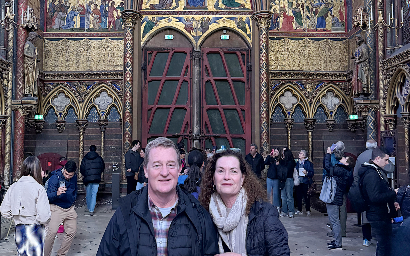 Visitors inside Sainte Chapelle, Paris, with ornate stained glass and Gothic architecture.