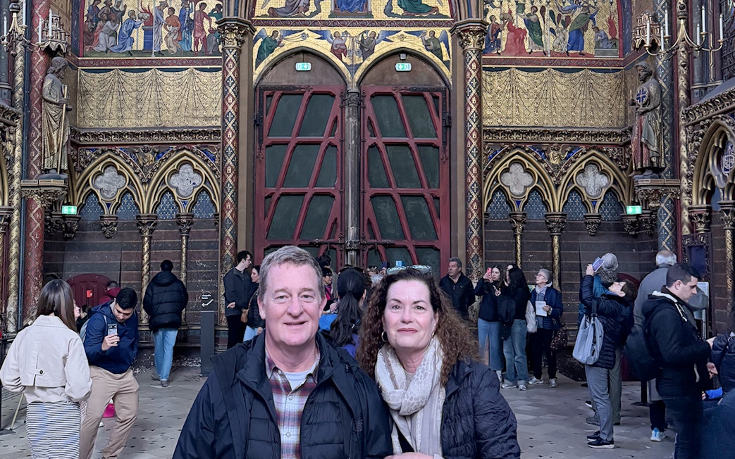 Visitors inside Sainte Chapelle, Paris, with ornate stained glass and Gothic architecture.