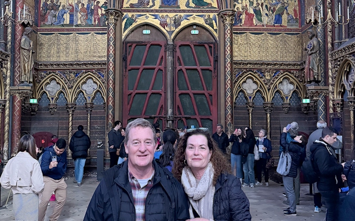 Visitors inside Sainte Chapelle, Paris, with ornate stained glass and Gothic architecture.