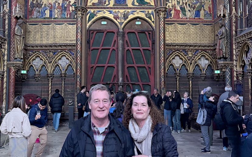 Visitors inside Sainte Chapelle, Paris, with ornate stained glass and Gothic architecture.